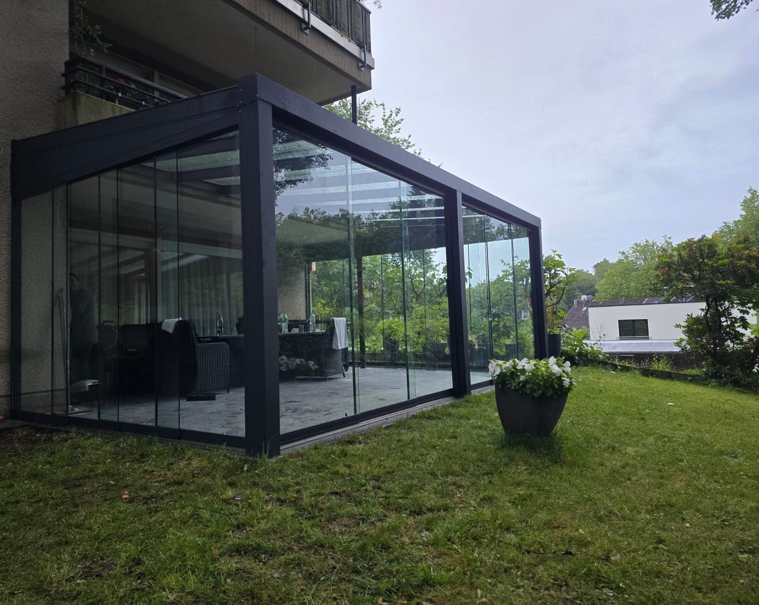 Glazen schuifwanden rondom een antraciet overkapping in de tuin
